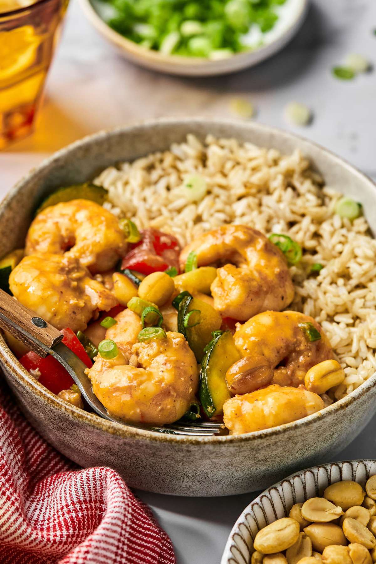 A bowl of kung pao shrimp with brown rice and a fork.