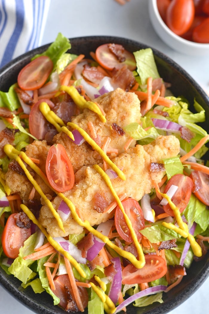 Paleo Honey Mustard Chicken Salad! Crispy almond flour tenders served over a bacon salad with a lightened up honey mustard dressing. A healthier mustard chicken that's family approved! Gluten Free + Paleo + Low Calorie