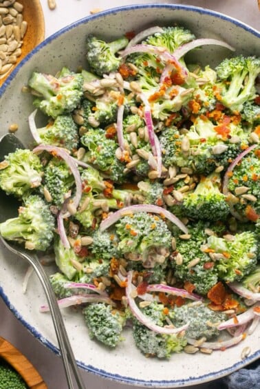 A bowl of healthy broccoli crunch salad surrounded by small bowls of ingredients.