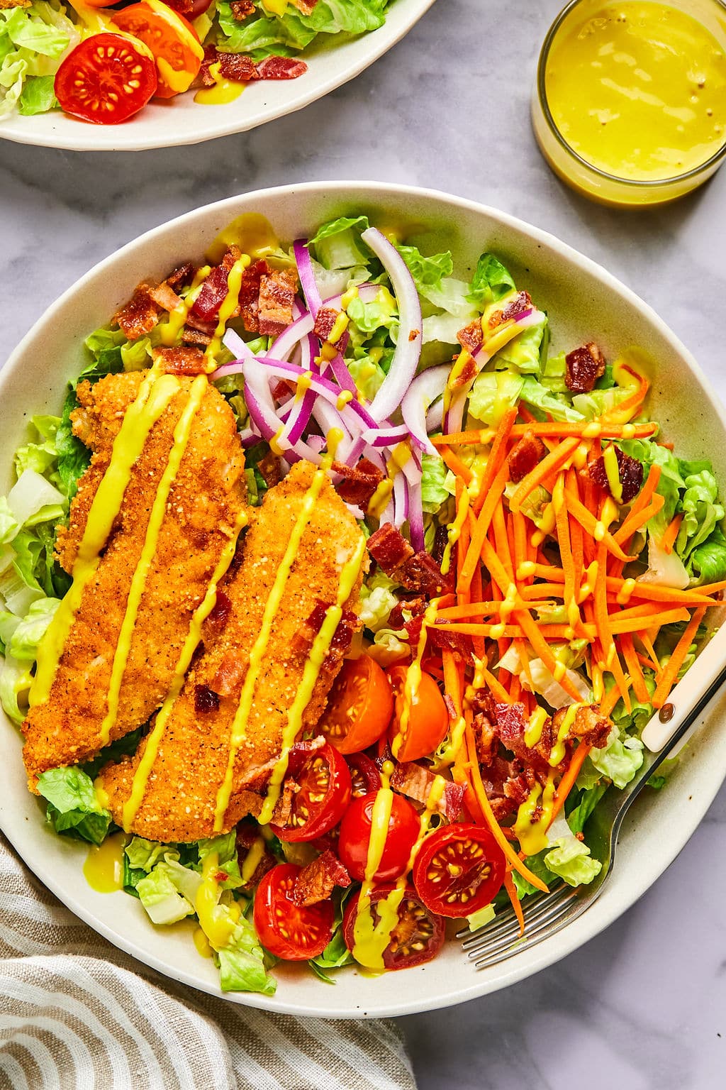Crispy chicken tender salad drizzled with honey mustard over lettuce with vegetables.