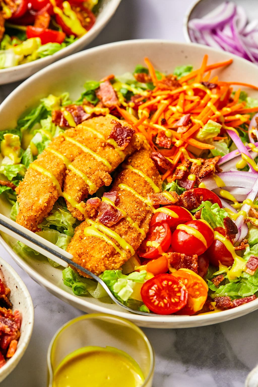A salad topped with two crispy chicken tenders and colorful veggies.