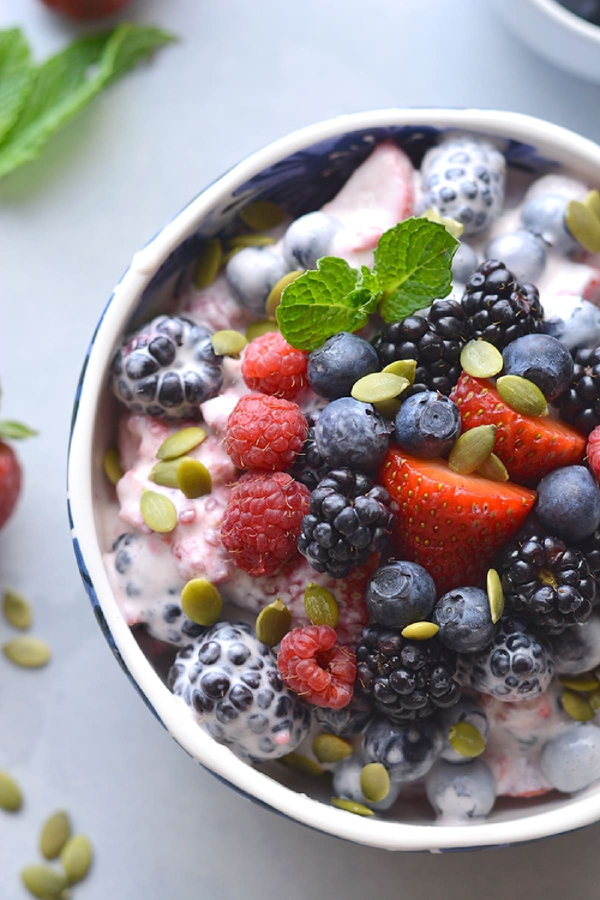 fruit salad with berries in a white bowl on a white table.