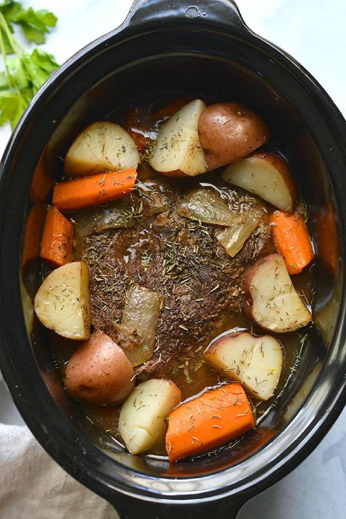 cooked pot roast in a slow cooker with carrots and sliced potatoes.