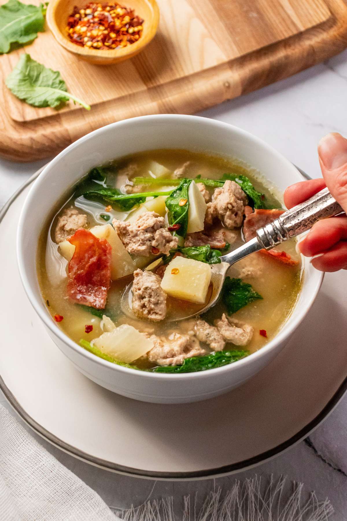 A bowl of skinny zuppa toscana with a hand dipping a spoon into the bowl.