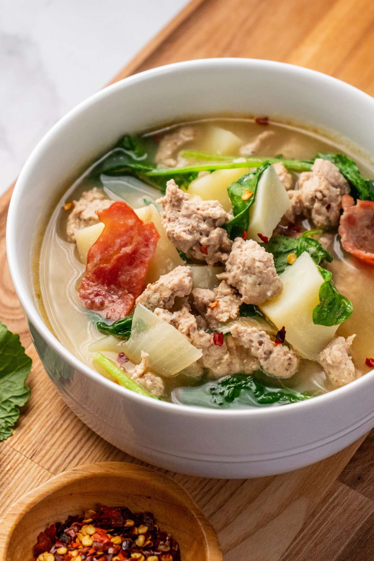 A bowl of healthy zuppa toscana on a wooden board and topped with red pepper flakes.