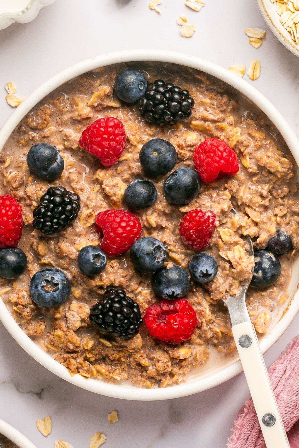 A bowl of protein oats on the table topped with berries and a spoon in the bowl.