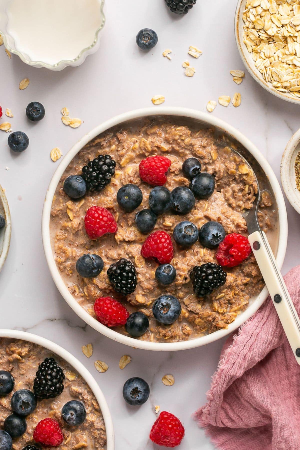 A bowl of chocolate protein oatmeal on the table with blueberries, raspberries, and blackberries sprinkled on top.