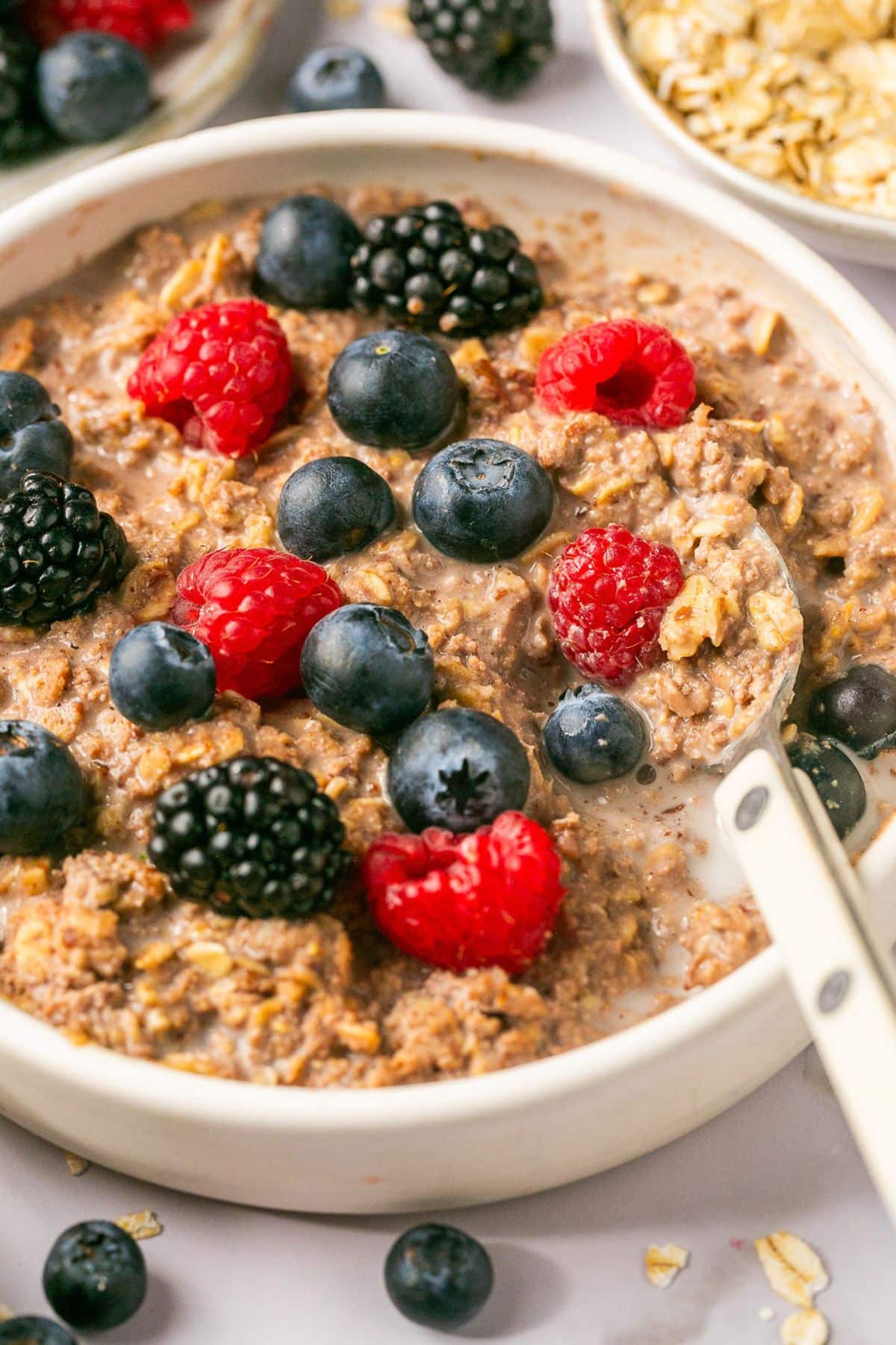 A bowl of high protein oats with a spoon scooping up a bite and berries on top.