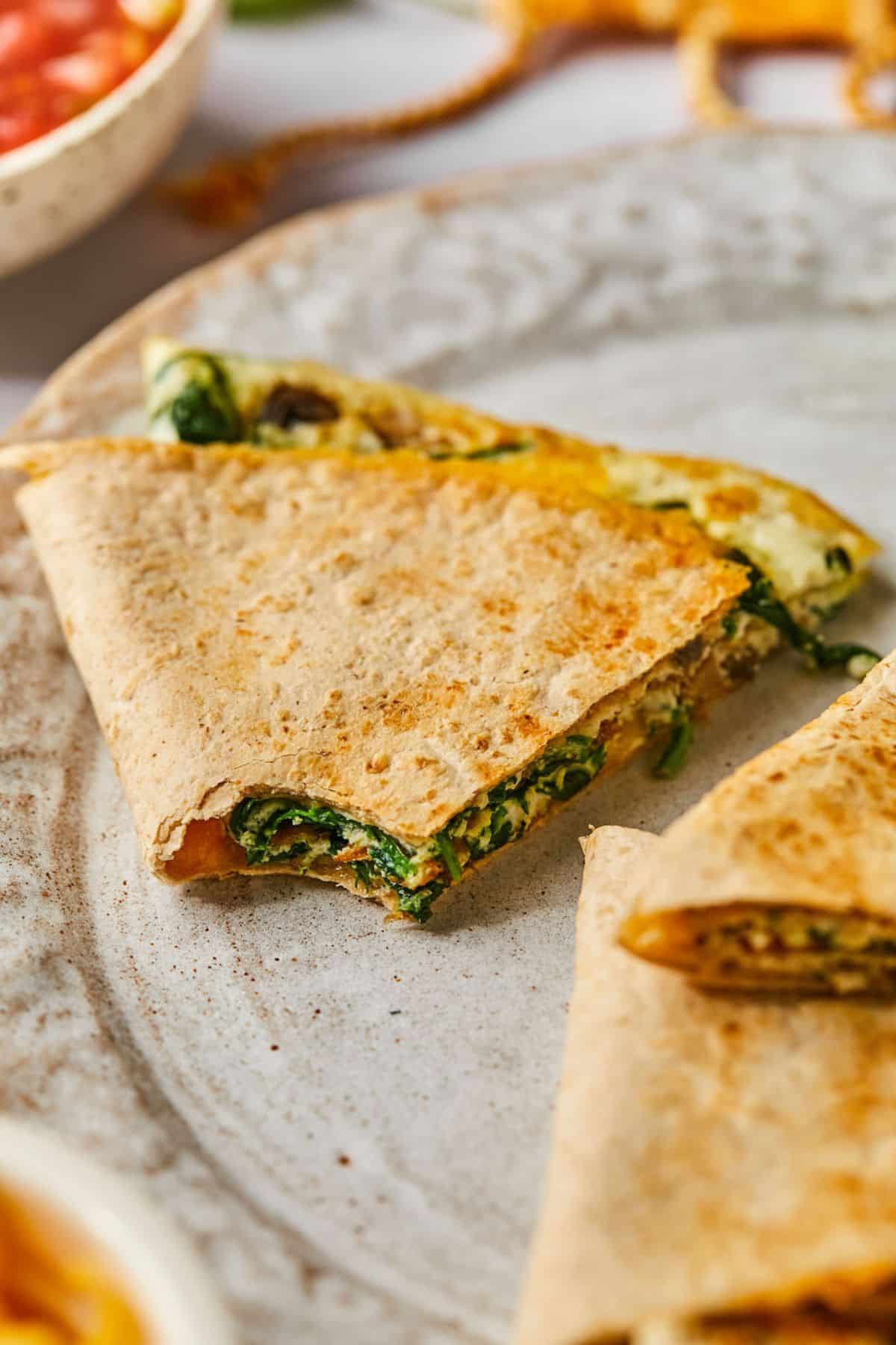A healthy quesadilla on a plate with a bite missing.