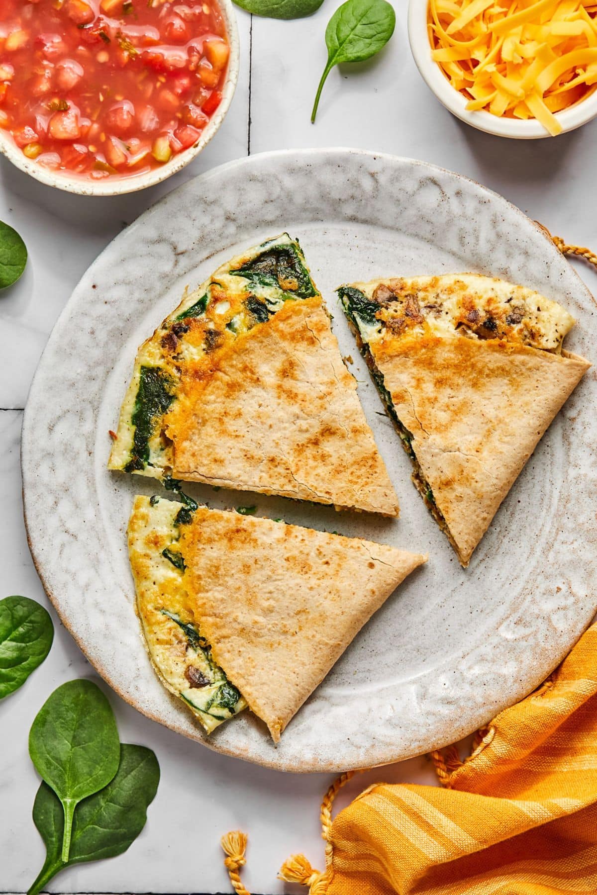 A high protein breakfast quesadilla cut into triangles on a plate with a bowl of sausage and cheese to the side.