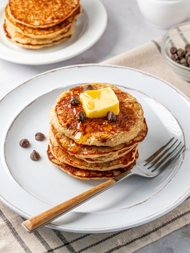 A stack of banana oat pancakes on a plate topped with butter and a few chocolate chips.