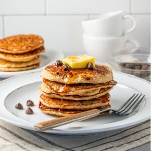 A stack of banana oat pancakes on a plate topped with a slice of banana.