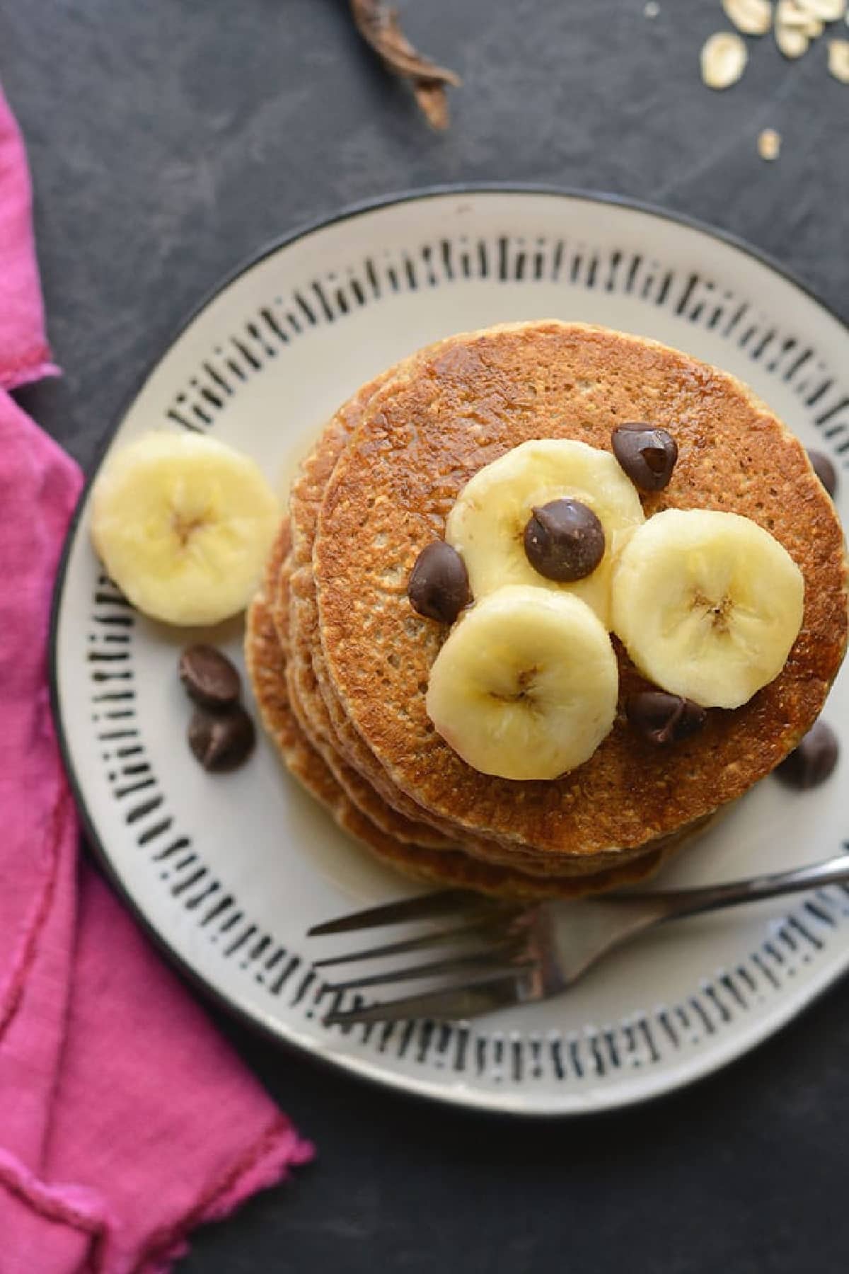 pancakes on a white plate with sliced bananas on top and fork.