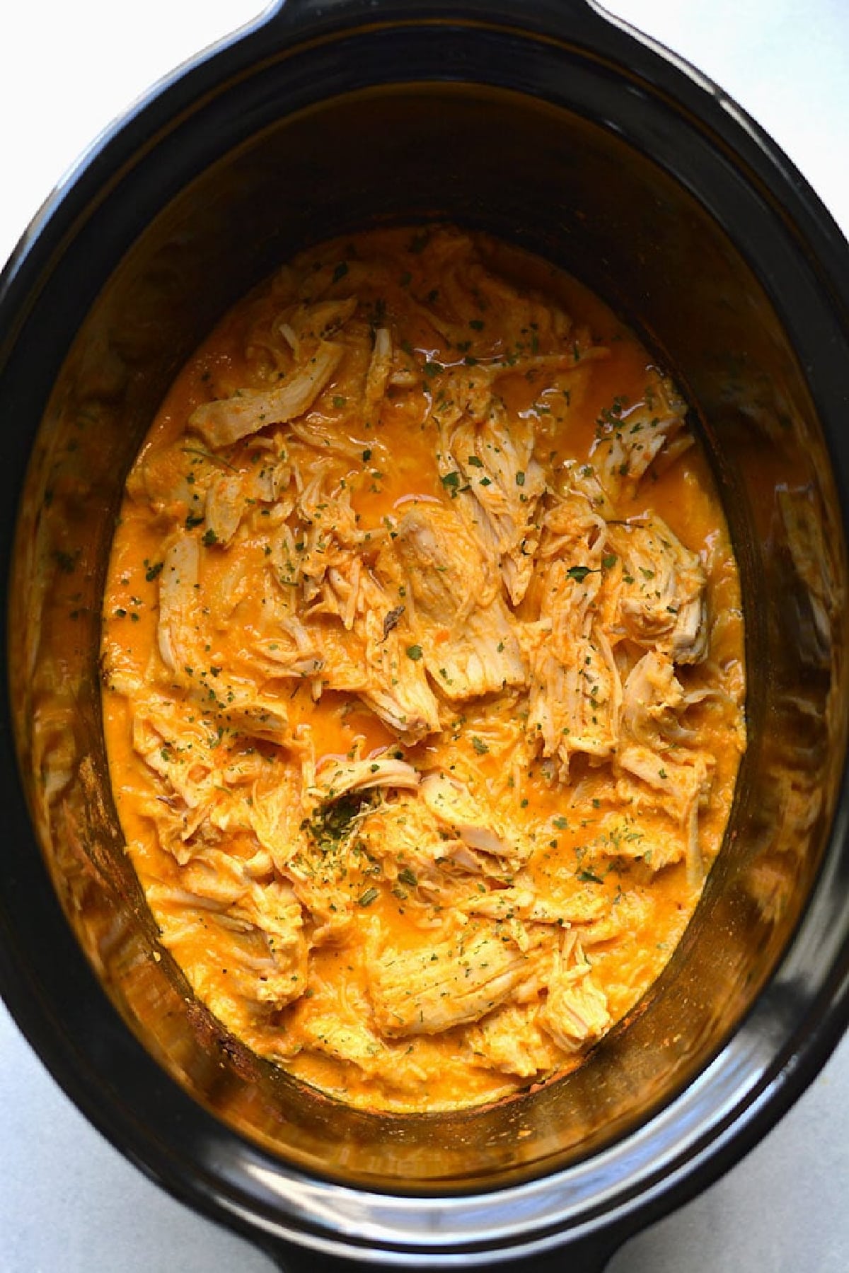 cooked chicken with buffalo sauce in a slow cooker.