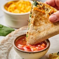 A hand dipping a healthy breakfast quesadilla into a bowl of salsa.