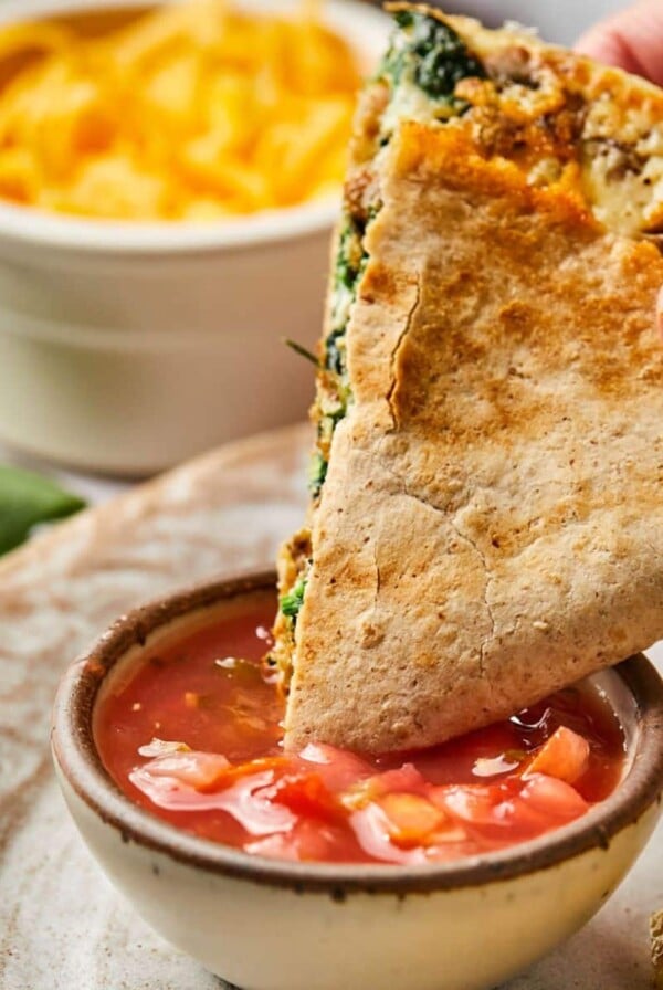 A hand dipping a healthy breakfast quesadilla into a bowl of salsa.