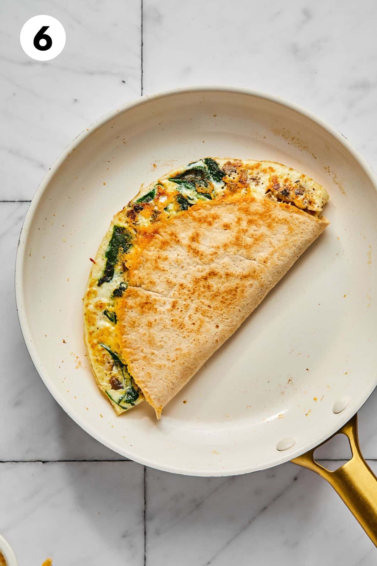 Tortilla folded in half to make a breakfast quesadilla cooking in a skillet.