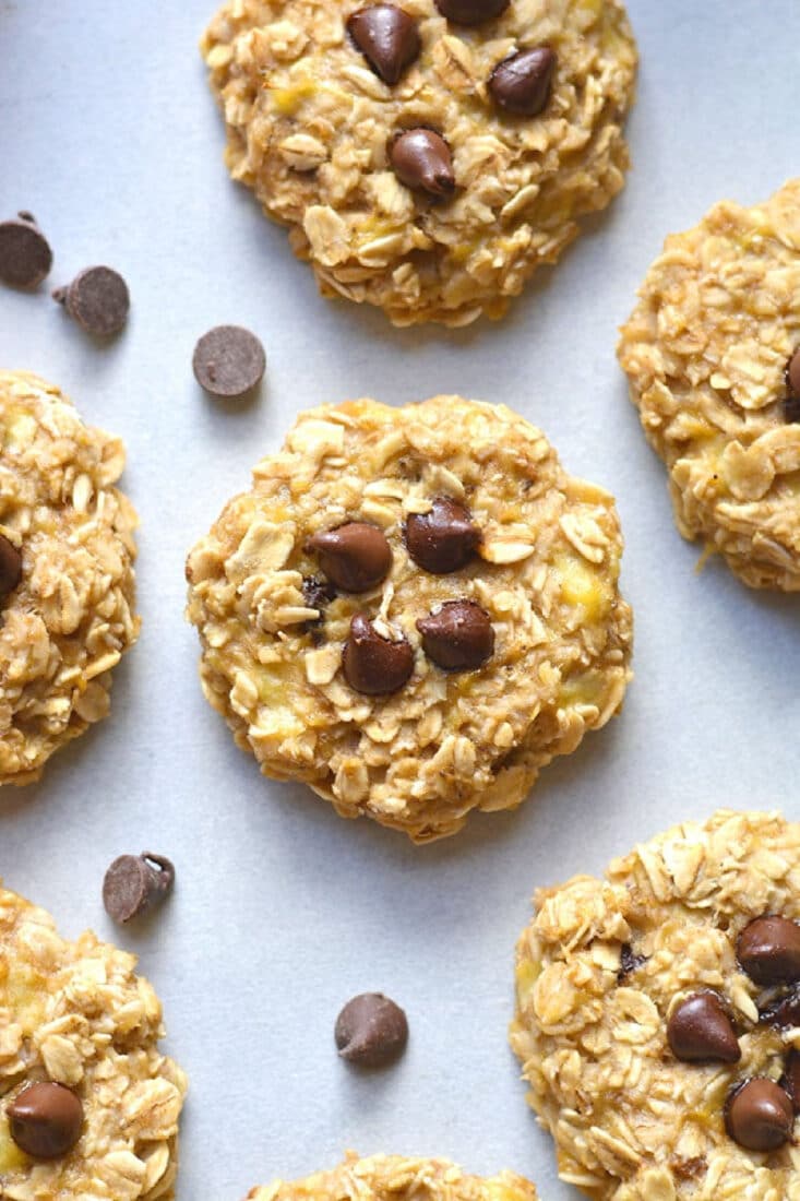 oatmeal chocolate chips cookies on a white surface with chocolate chips scattered nearby.