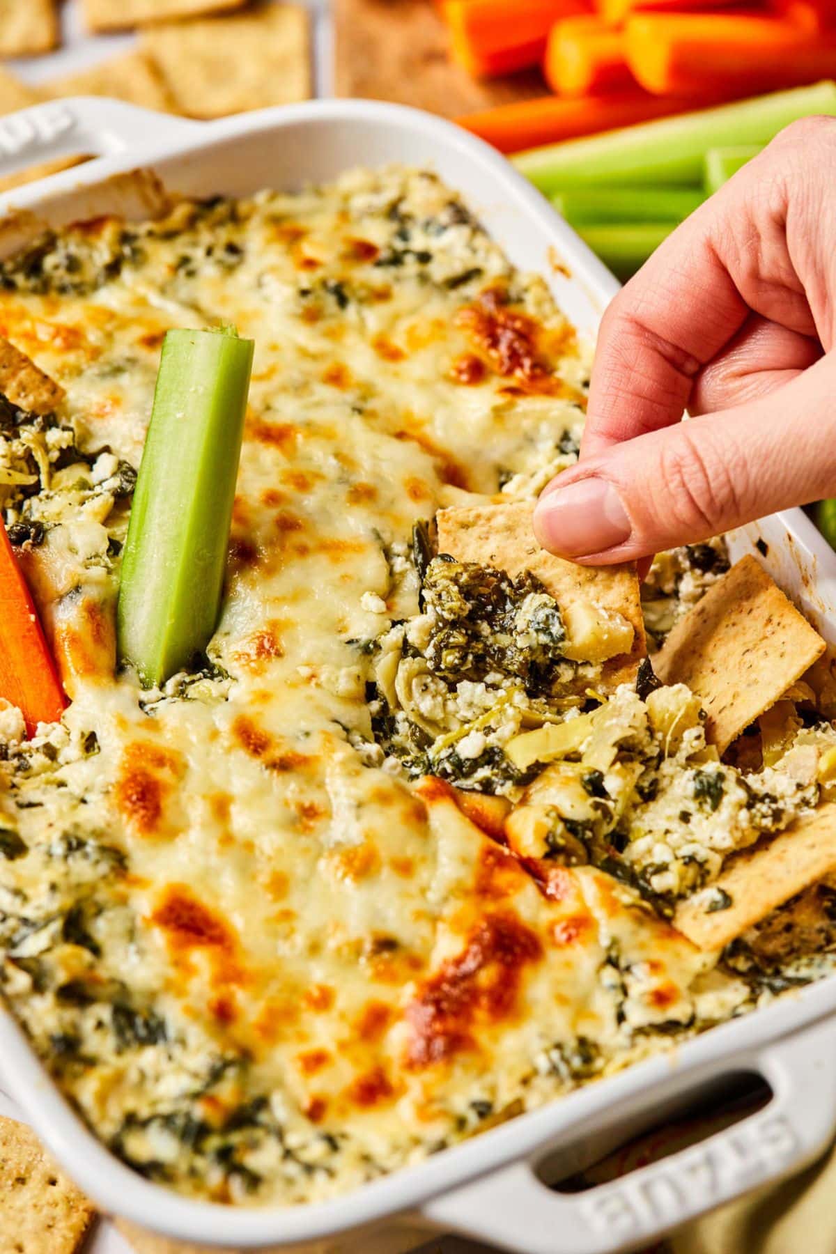 A hand reaching in a cracker to scoop up a bit of healthy spinach artichoke dip.