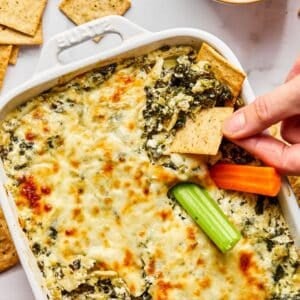 Cottage cheese spinach artichoke dip with a hand dipping a cracker.