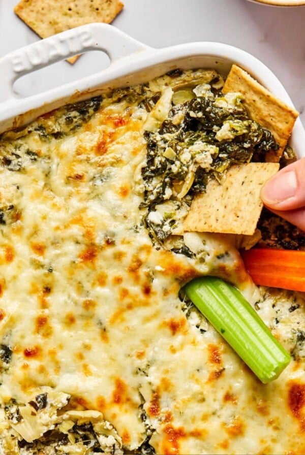 Cottage cheese spinach artichoke dip with a hand dipping a cracker.