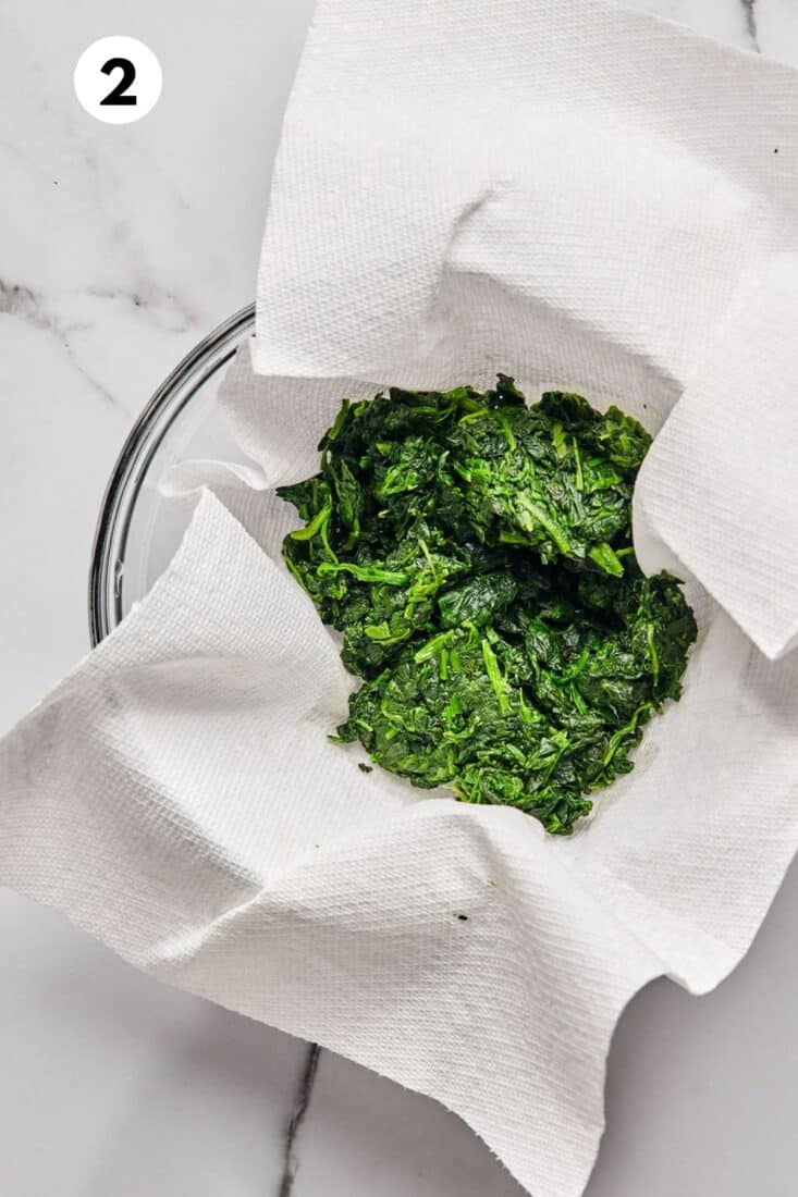 Spinach draining on a paper towel in a bowl.
