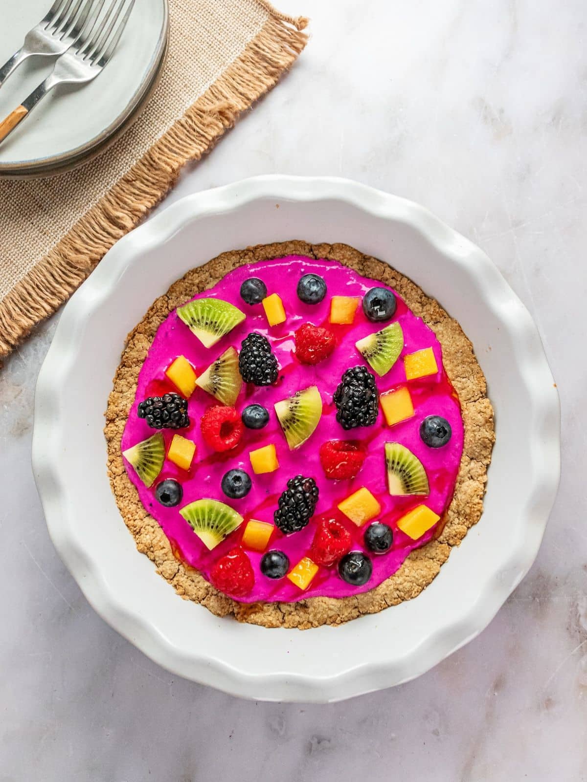 Fruit dessert pizza on a white and gravy surface.