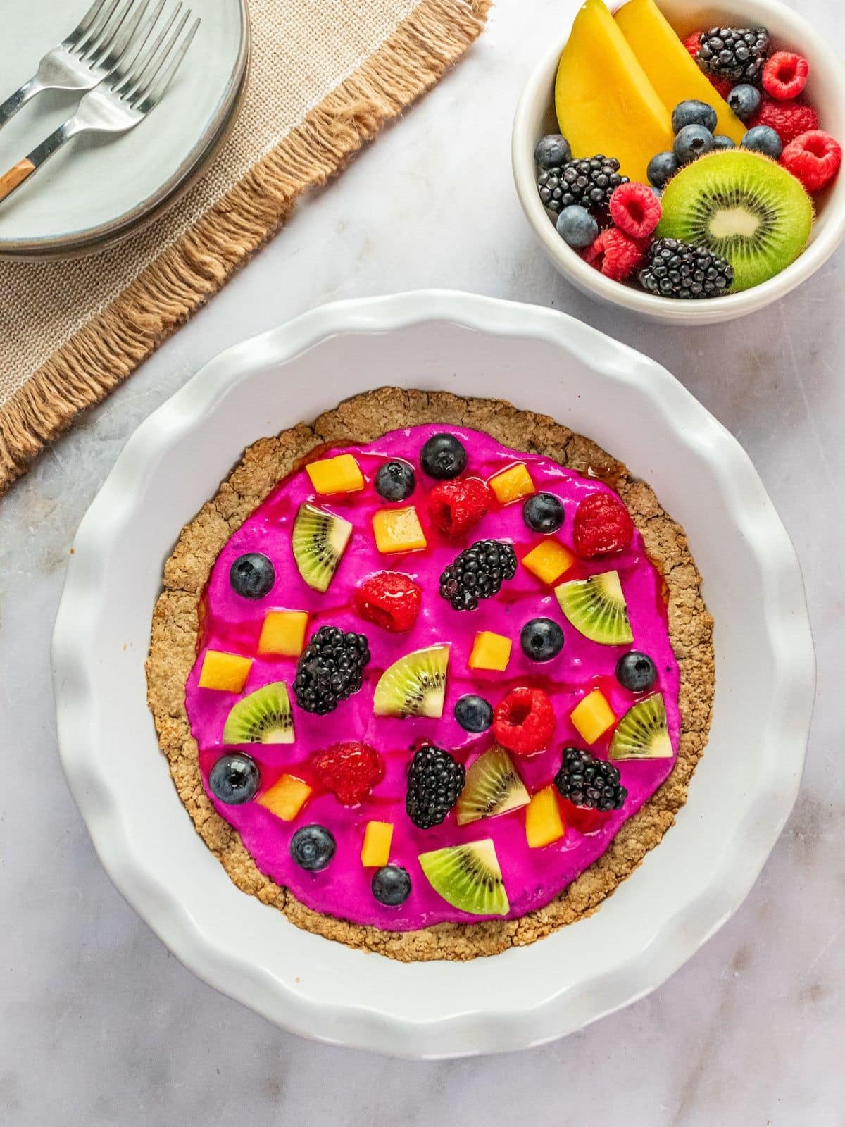 Healthy fruit pizza on a table with a bowl of fruit to the side.