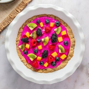 Healthy fruit pizza in a white pie dish on a table.