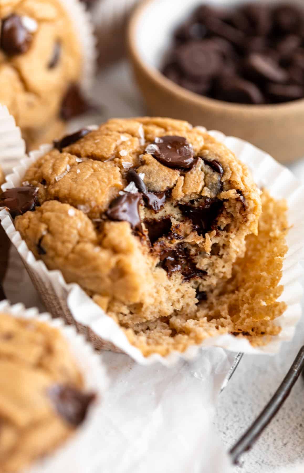 A banana oatmeal muffin with a bite missing and the paper pulled slightly away from the muffin.