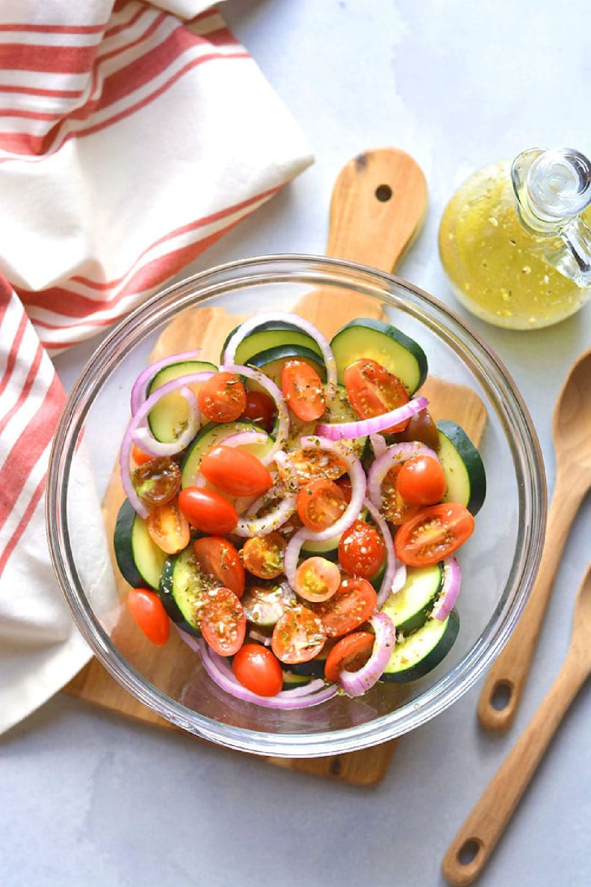 sliced tomatoes, sliced cucumber, red onion in a large clear bowl.