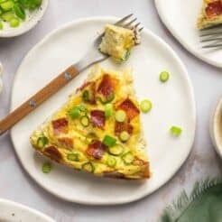 A slice of healthy quiche on a plate with a fork to the side holding a bite.