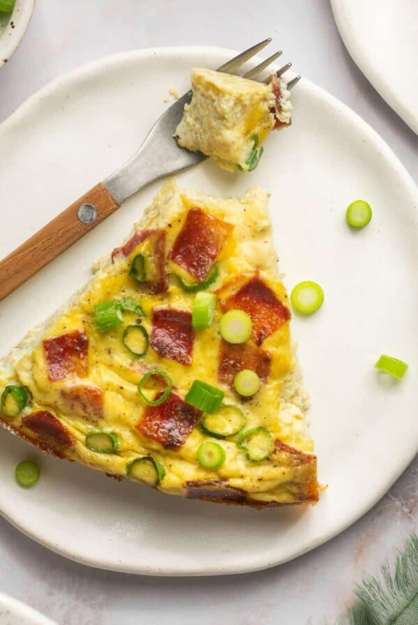 A slice of healthy quiche on a plate with a fork to the side holding a bite.