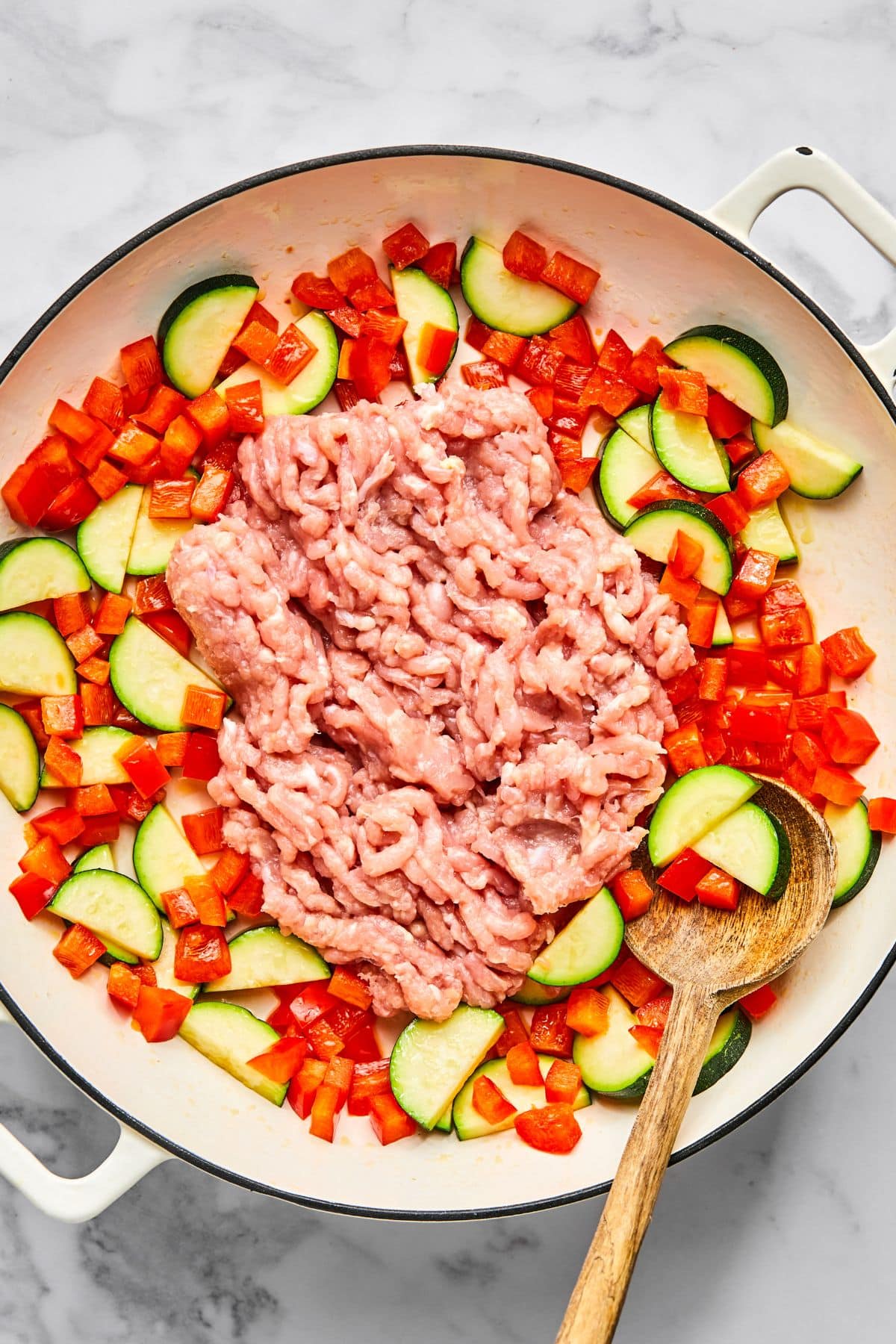 Vegetables and ground chicken added to a skillet to cook.