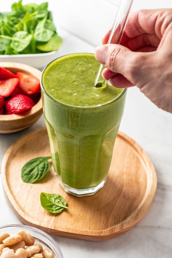 A hand adding a straw to a glass of a high protein high fiber smoothie.