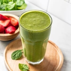 A high fiber smoothie on a wooden plate with bowls of spinach and strawberries to the side.