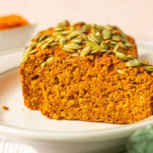 Pumpkin oat bread on a plate with a piece sliced to show the inside.