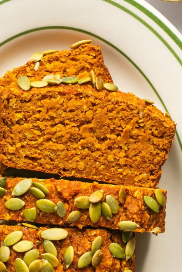 Slices of pumpkin oatmeal bread on a plate with some laying on their side.