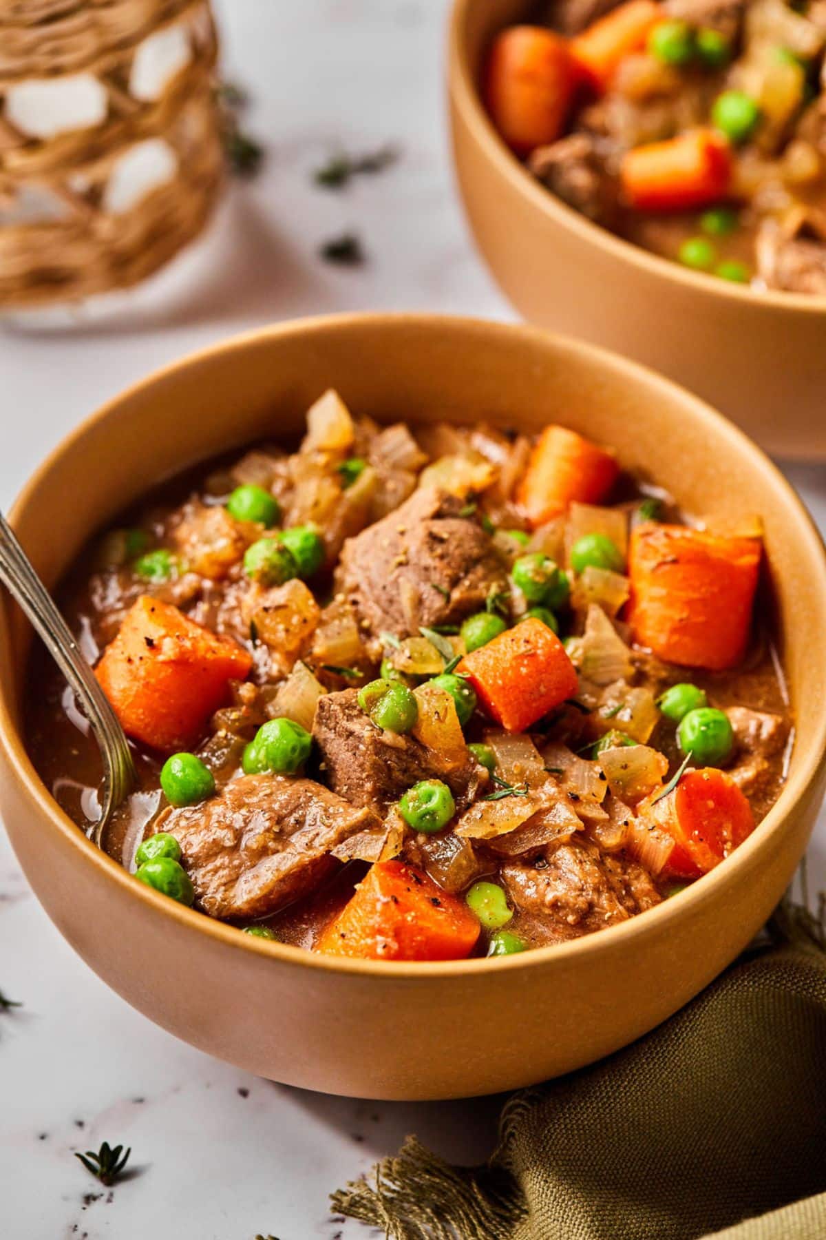 Bowls of healthy beef stew on the table with chunks of beef, carrots, and peas.