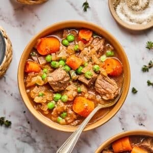 A bowl of crockpot beef stew on the table with a spoon in the bowl.