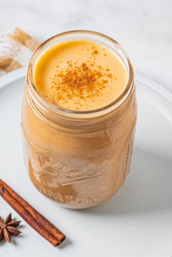 A pumpkin smoothie in a glass jar on a plate.