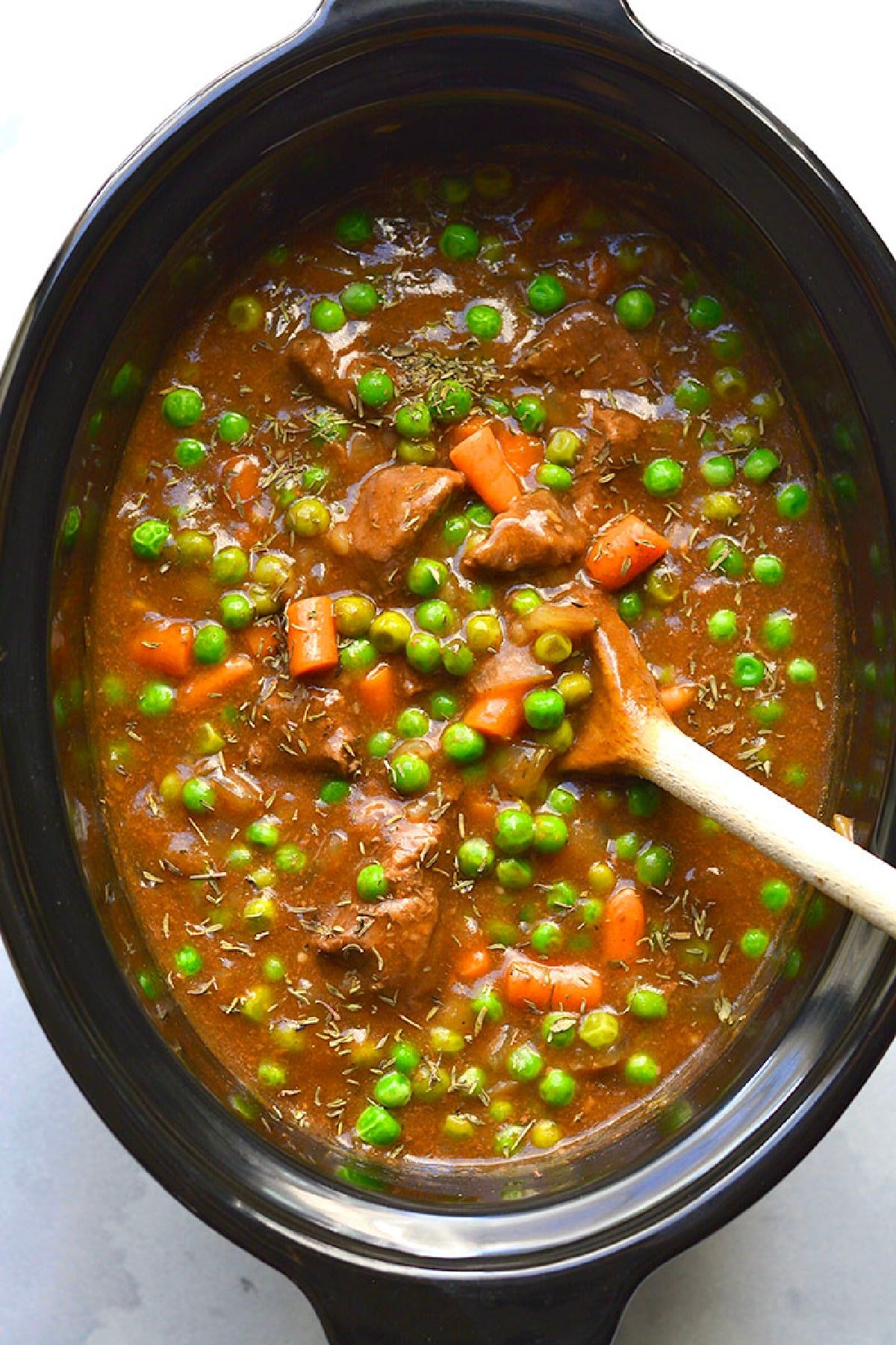 A crockpot of beef stew with a spoon in the crockpot.