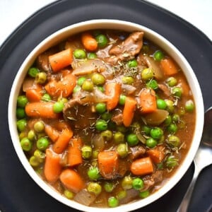 A white bowl with beef stew on a dark plate.