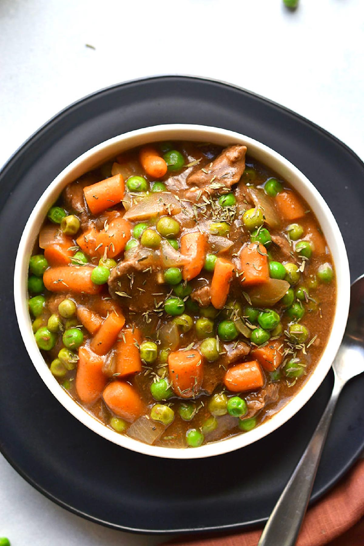 A white bowl with beef stew on a dark plate.