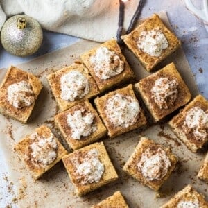 Eggnog cheesecake bars topped with whipped cream on a table.