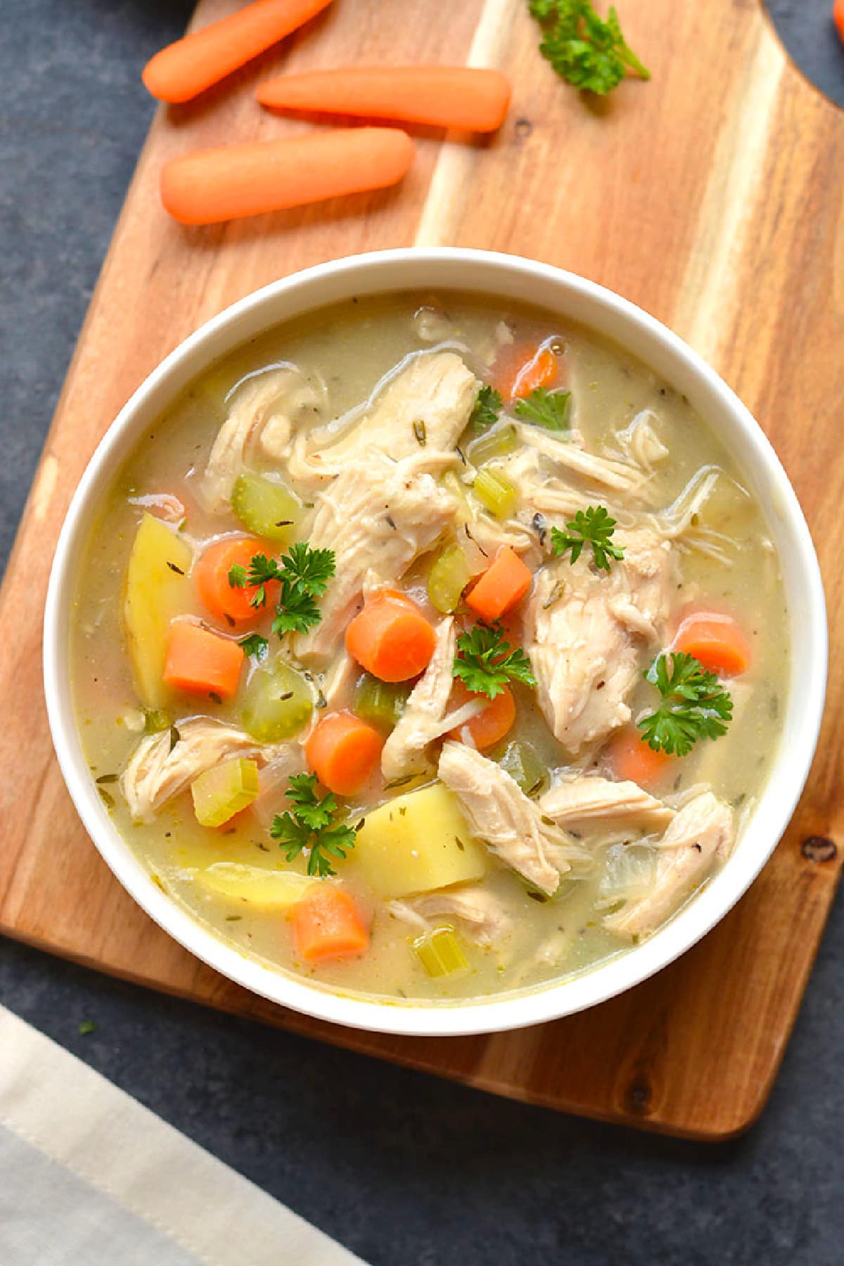 A bowl of chicken pot pie soup on a brown cutting board.