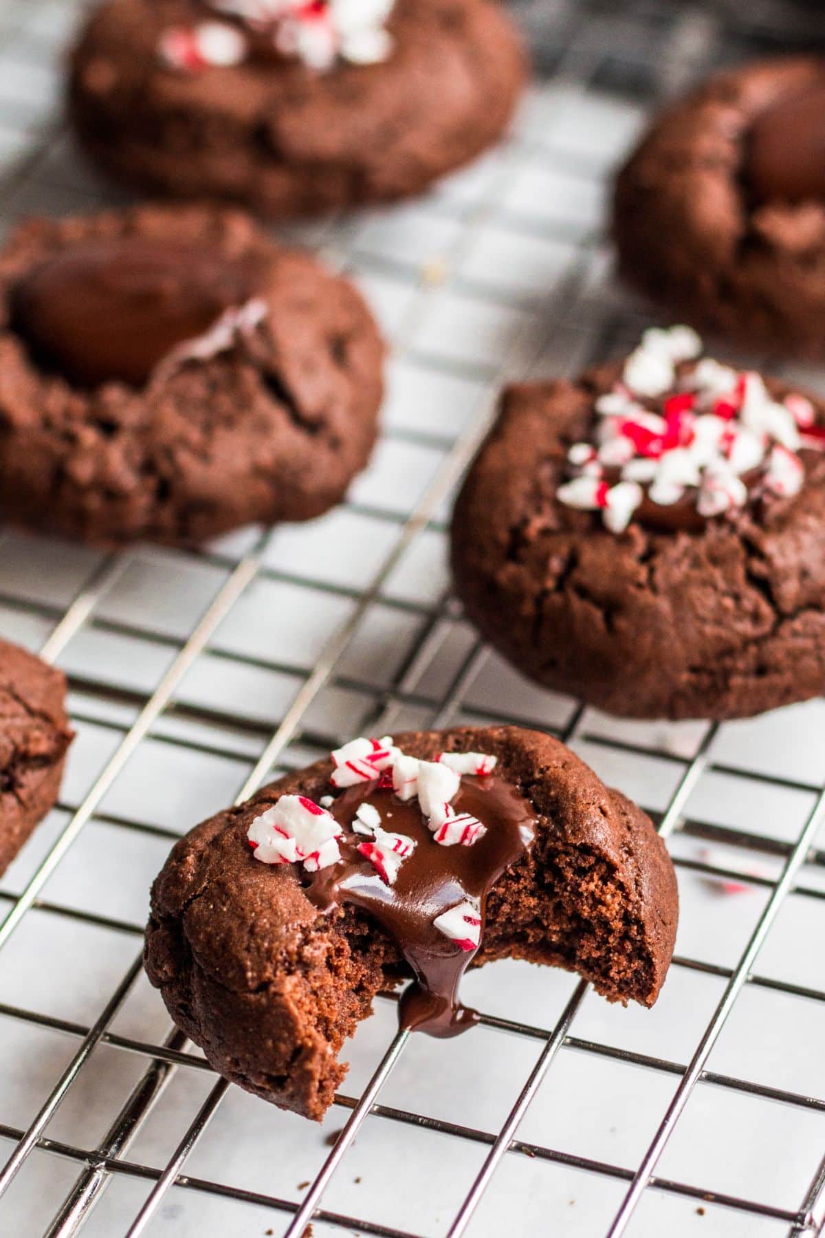 Chocolate thumbprint cookies on a cooling rack with one that has a bite taken out.