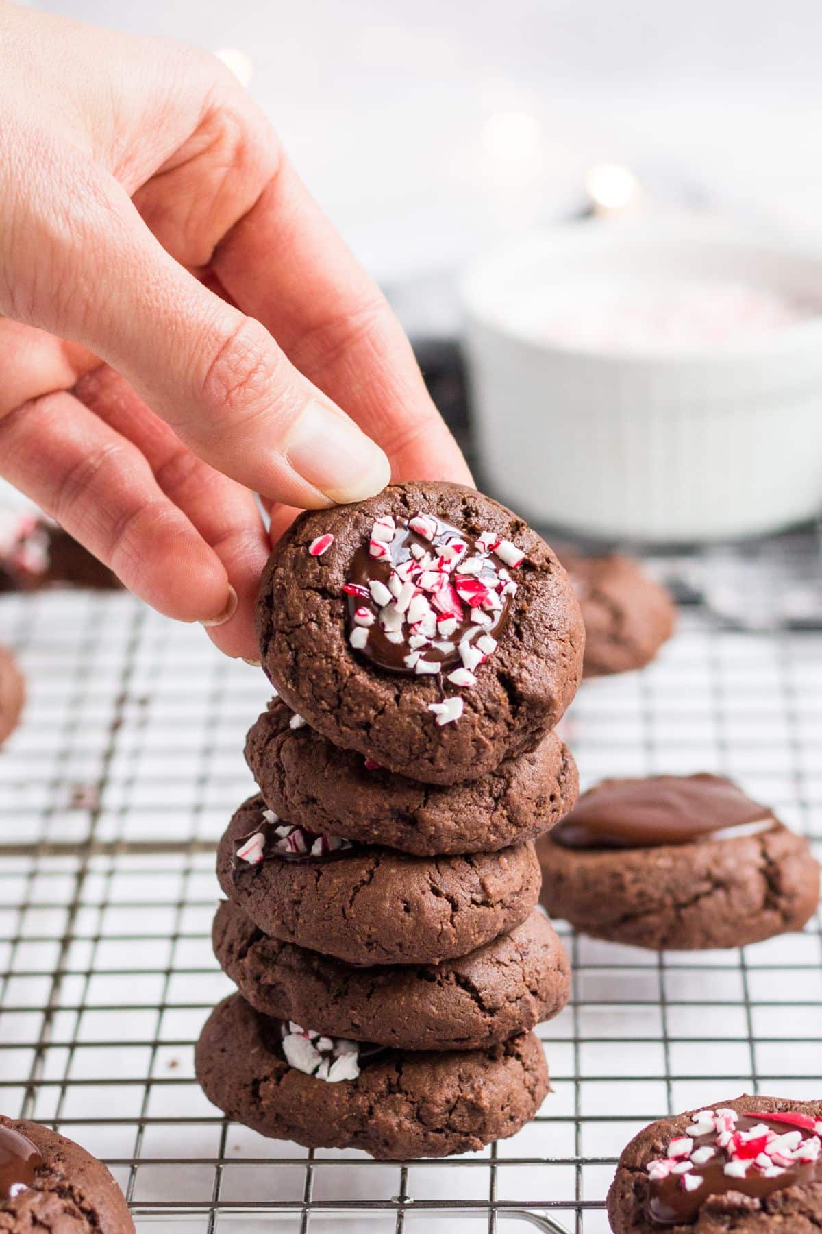 A hand picking up a cookie off a stack of chocolate thumbprint cookies.
