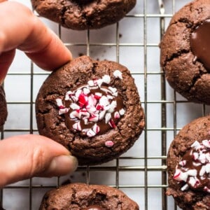 Chocolate thumbprint cookies on a cooling rack with a hand picking one up.