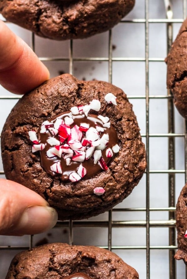 Chocolate thumbprint cookies on a cooling rack with a hand picking one up.